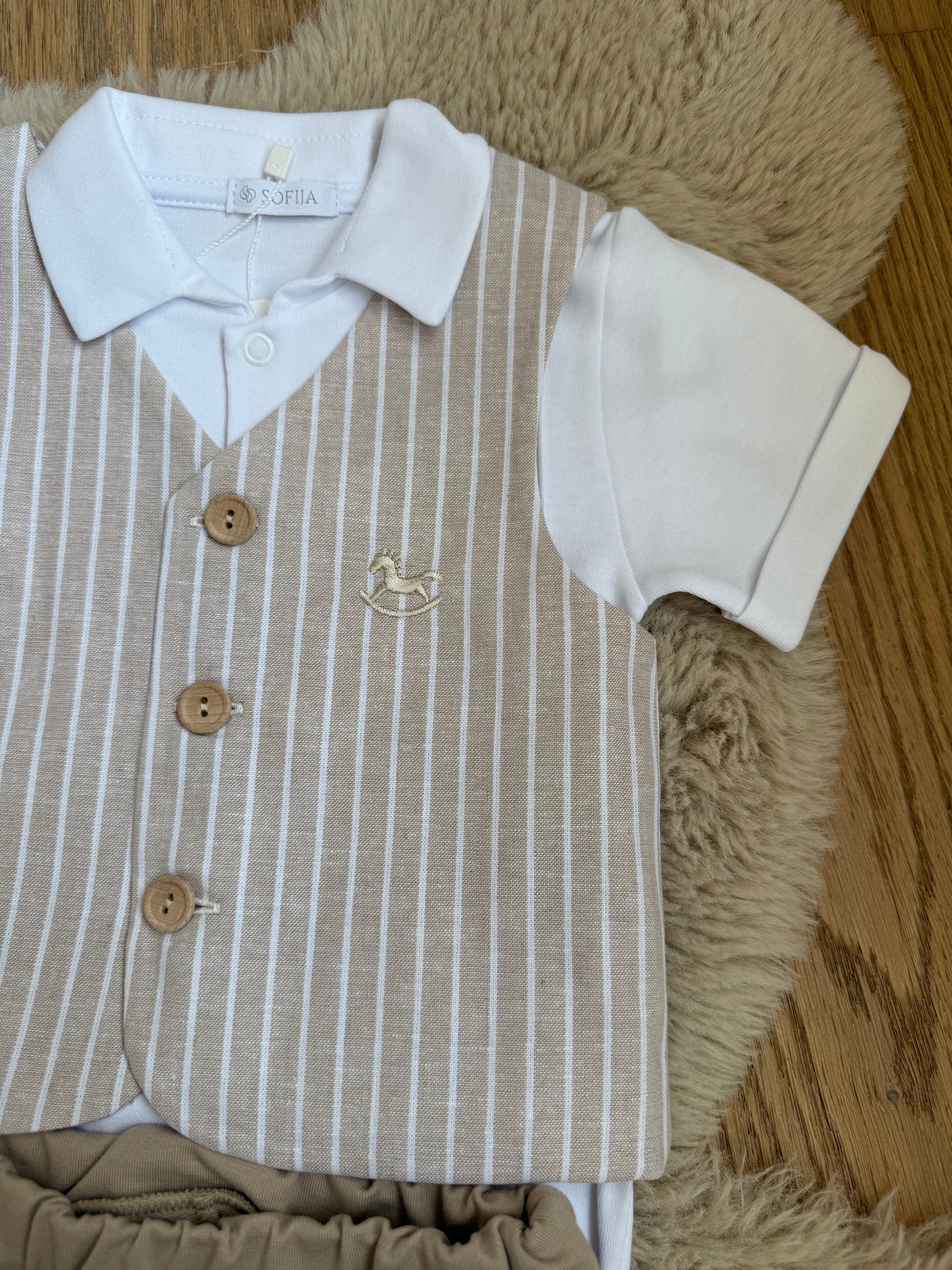 Detail van beige babykostuum jasje met subtiel hobbelpaard accent